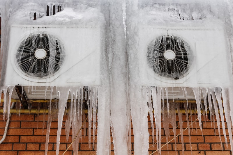 Two mounted outdoor AC units freezing up due to being covered in ice.