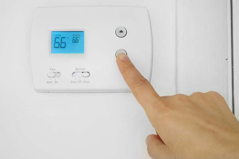 Homeowner adjusting thermostat to represent why an AC unit is turning on and off.