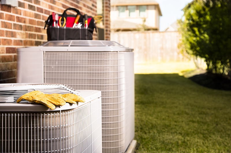 Two outdoor HVAC systems with maintenance tool bags and gloves sitting on top of them.
