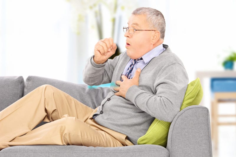 Male homeowner coughing on his couch due to poor ventilation and air quality in his home.