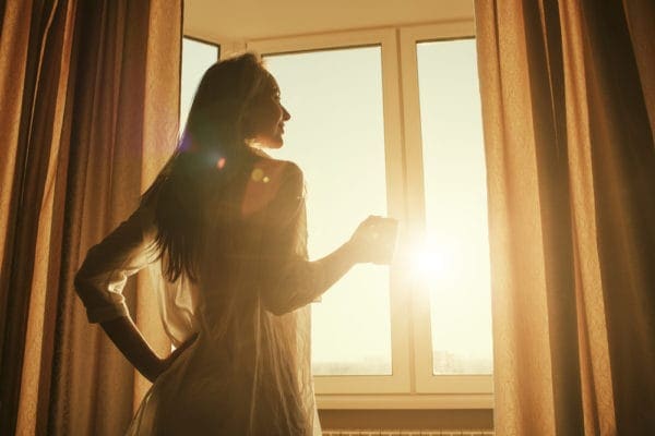 Young woman enjoying the morning during sunrise to represent peace of mind with your HVAC system.