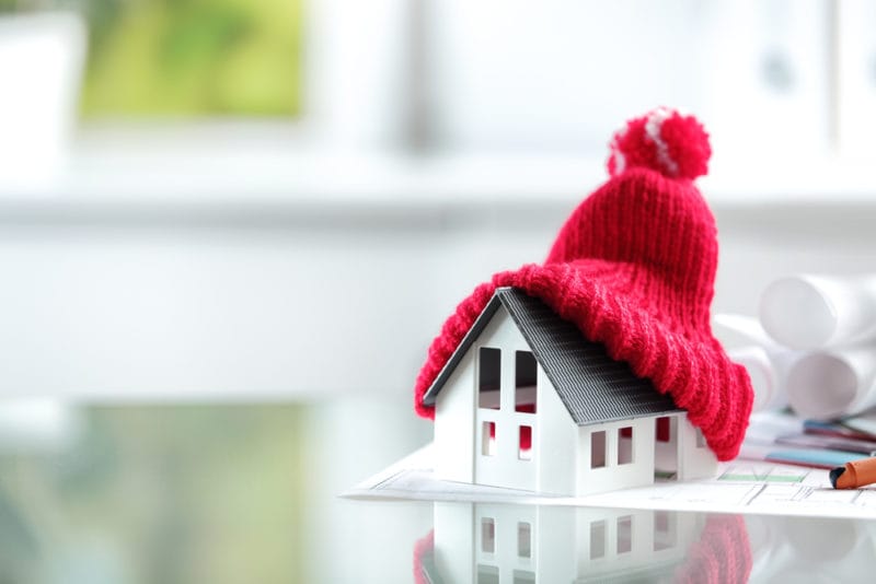 Miniature home with beanie on top of it to represent information about needing good insulation year-round.