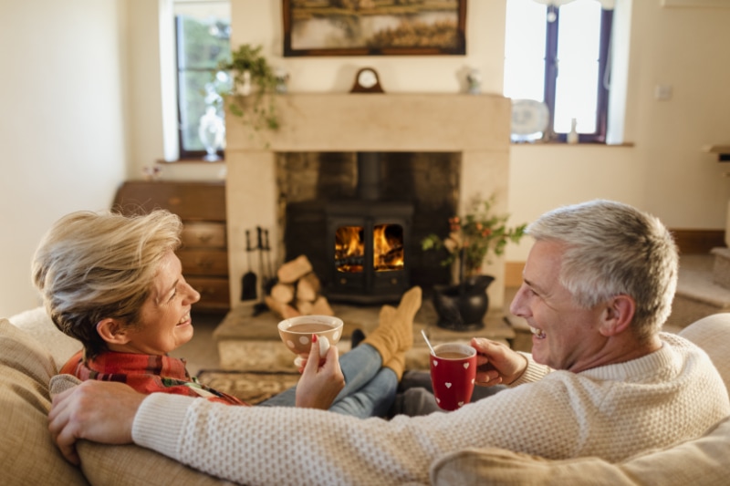 Retired couple sitting in front of a fire discussing lowering their winter heating bill.