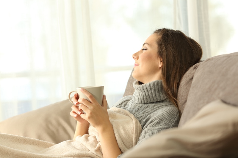 Female homeowner relaxing on her couch after a zone control system was installed in her home.