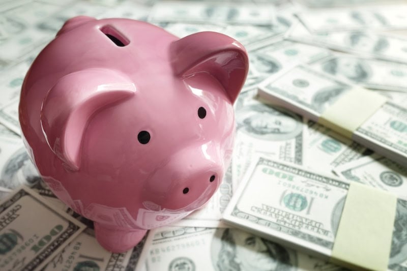 Pink piggy bank sitting on stacks of hundred dollar bills representing lowering your heating bill.