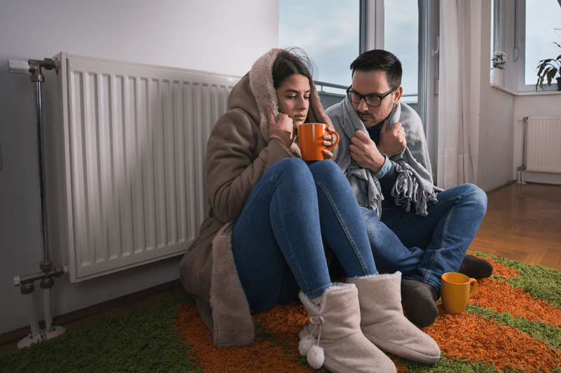 Couple in living room wearing coat and blanket to represent when it's time to buy a new furnace.