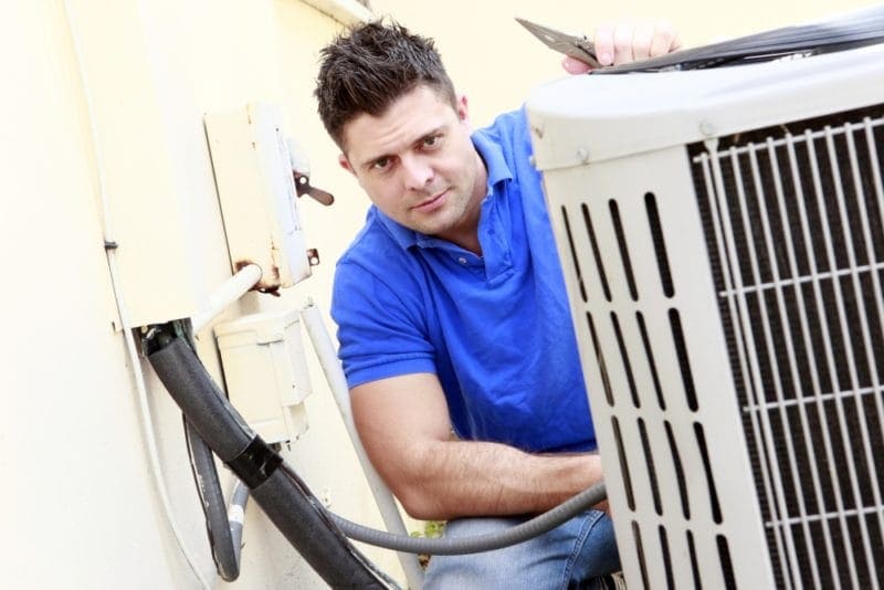 HVAC technician working on outdoor air conditioner to represent three things your air conditioning unit is trying to tell you.