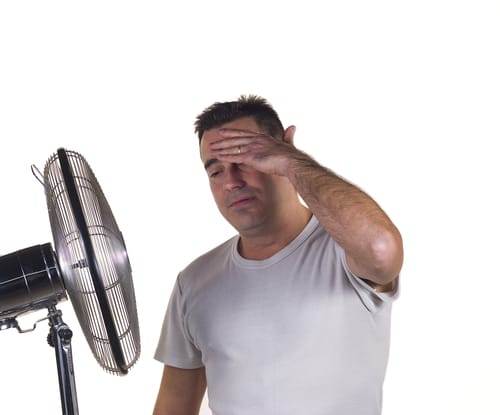 Man trying to cool off in front of an osculating fan due to AC troubles.